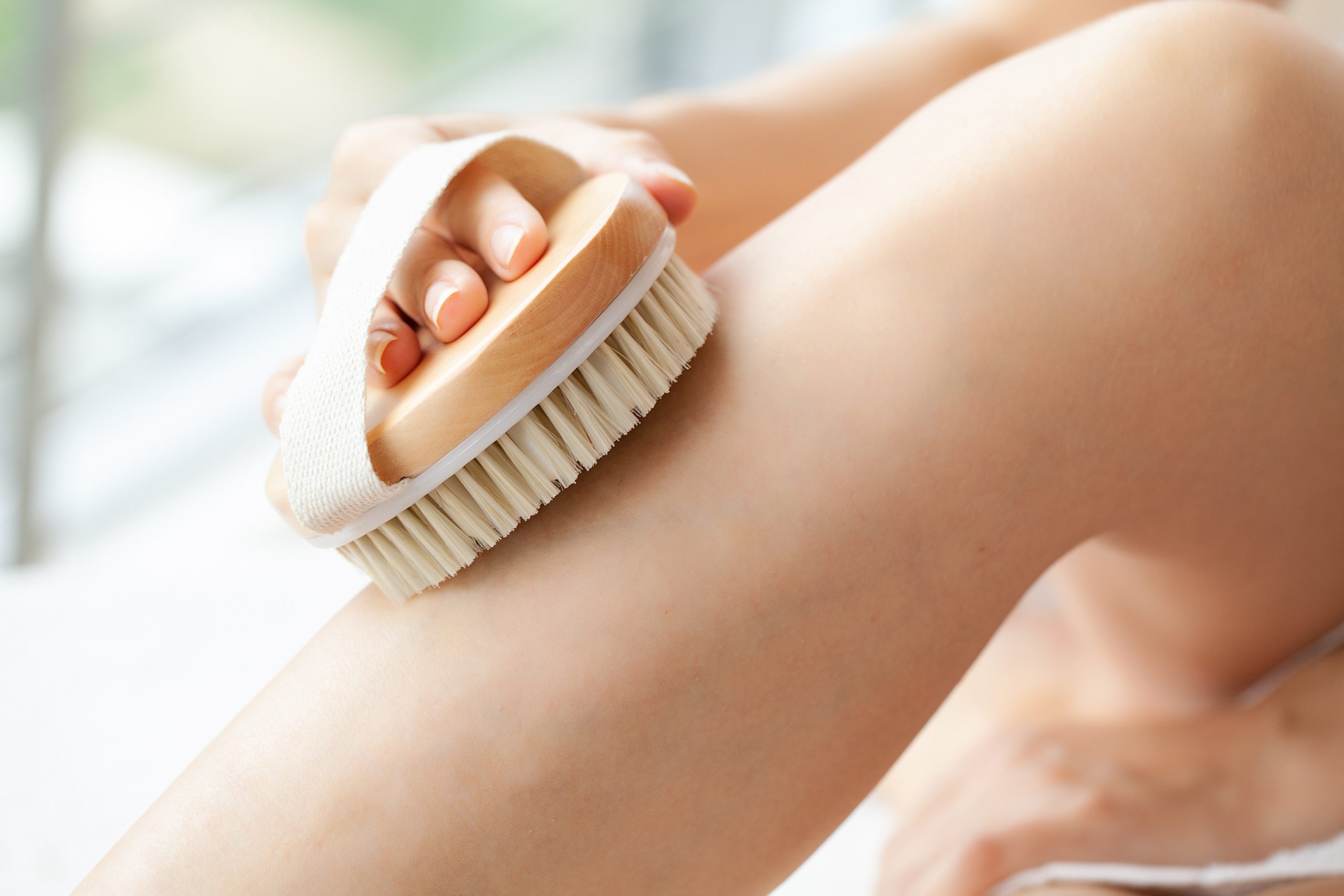 Cellulite treatment, woman arm holding dry brush to of her leg.