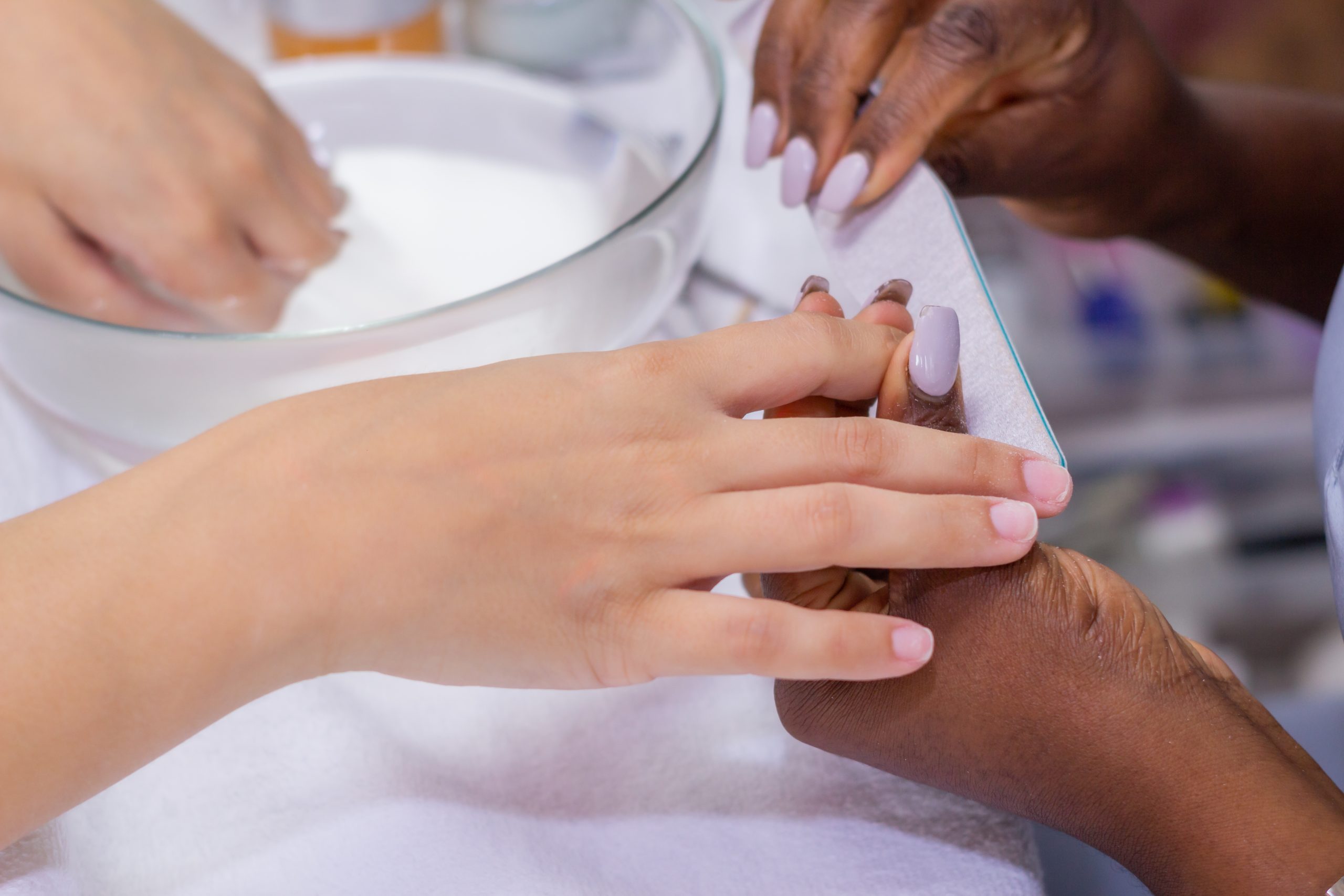 manos-manicuristas-aplicando-las-unas-del-cliente-femenino-con-un-tampon-blanco-en-el-salon-de-unas