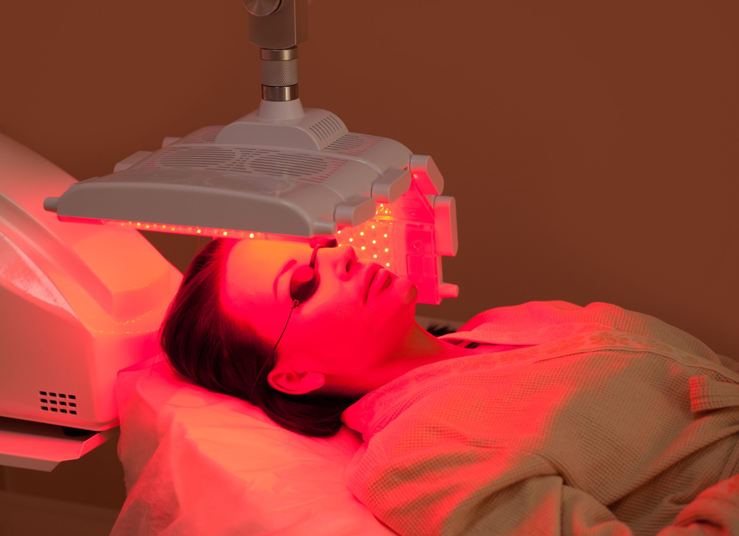 Woman lying on a table with protect glasses on eyes have a skin treatment under beauty device. Beauty spa salon.